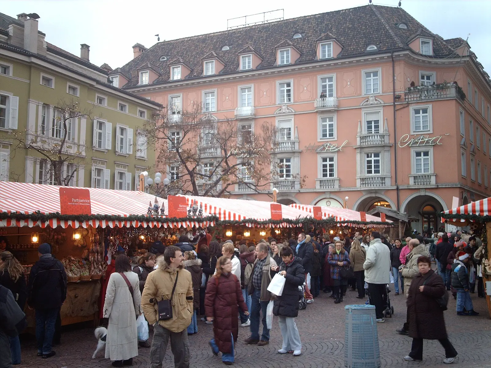 Visitors browsing the striped market stalls of the Christmas market in Bolzano beside pastel townhouses