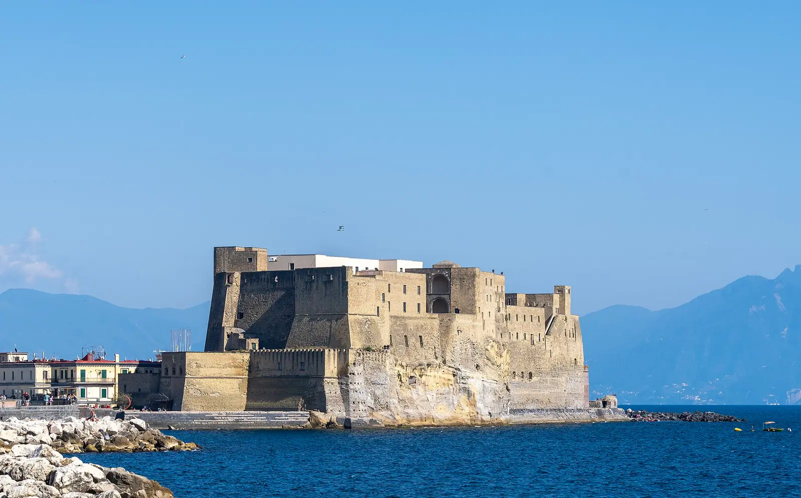 The Castel dell'Ovo fortress on a rocky promontory in the Bay of Naples under a blue sky