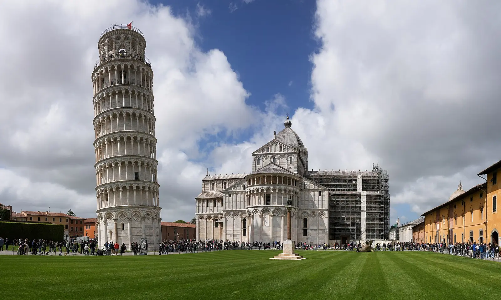 The Leaning Tower and the Cathedral on the lawn of Piazza dei Miracoli in Pisa under a cloudy sky