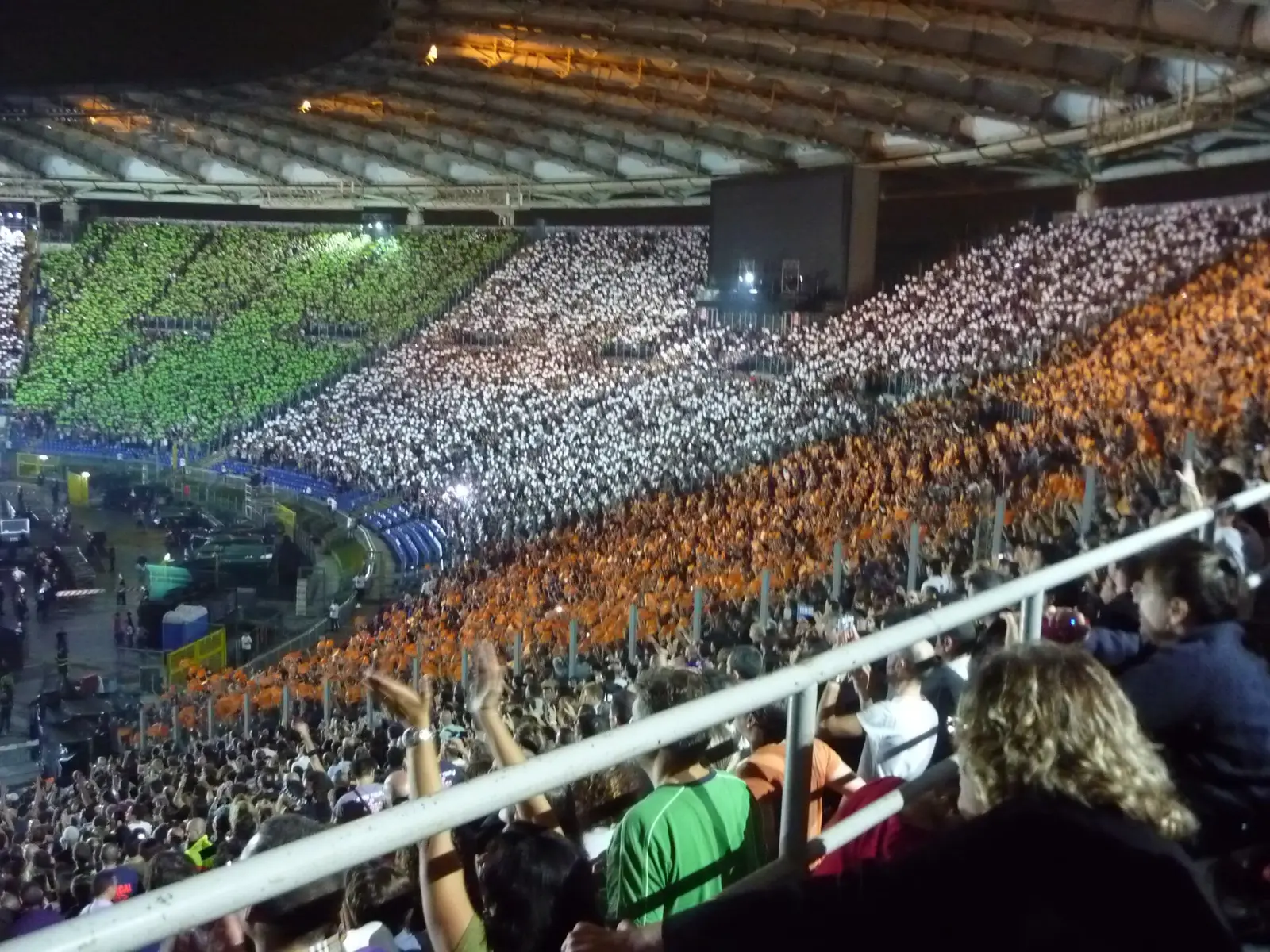 A packed Stadio Olimpico stand lit in orange and green during a concert