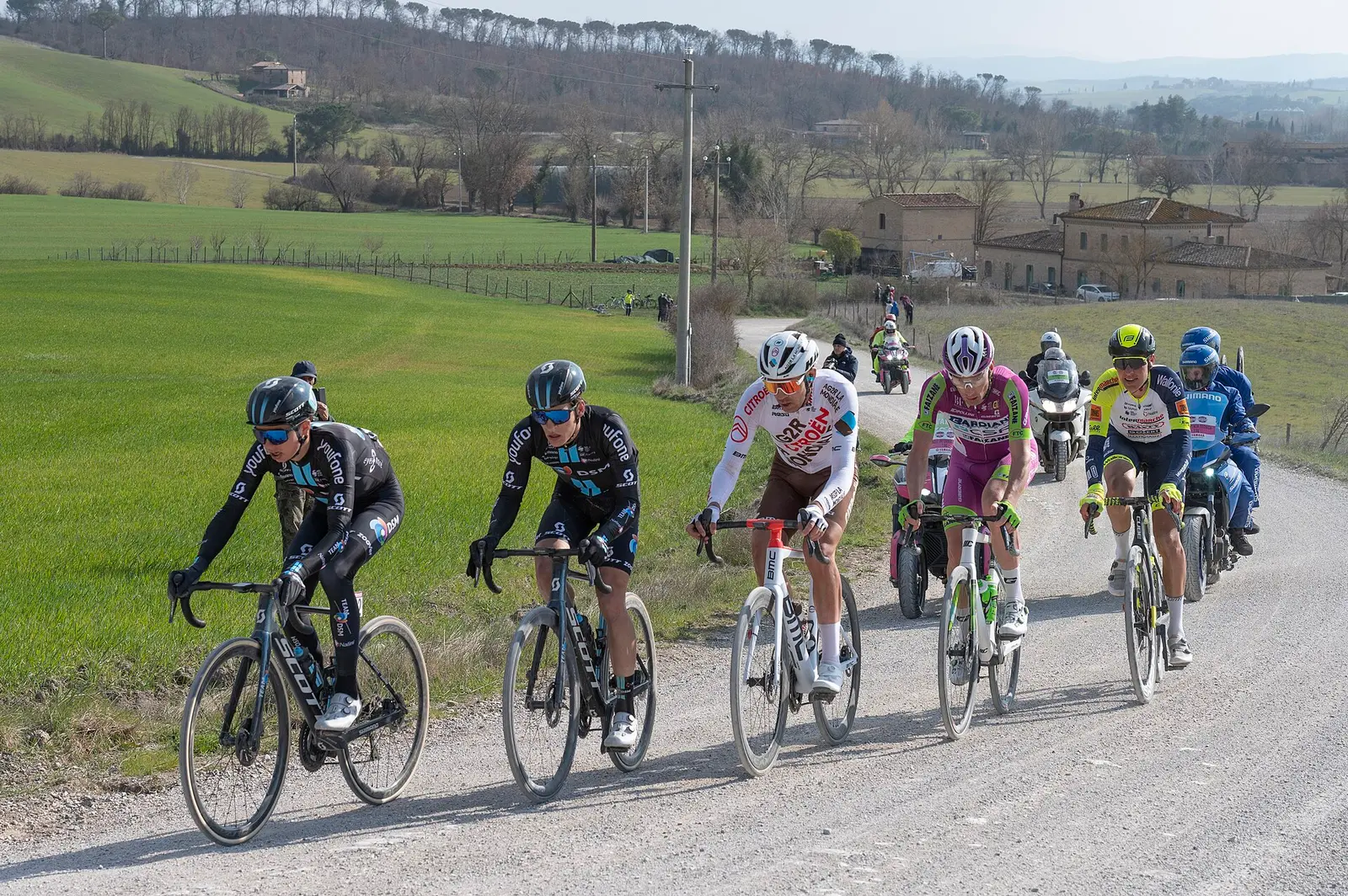 Riders on a white gravel road through green Tuscan hills during Strade Bianche in 2022